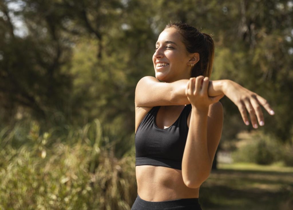 mulher sorridente se alongando e fazendo exercicios para cuidar da saúde