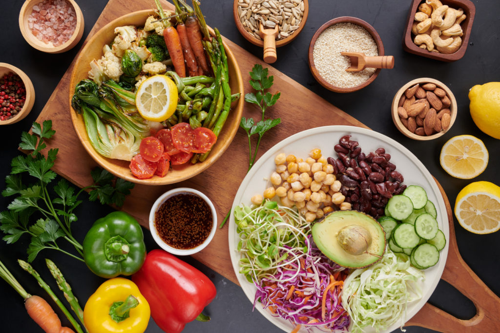 uma mesa de madeira vista de cima com vários potes de salada, vegetais e grãos. Ingredientes necessários para cuidar da saúde