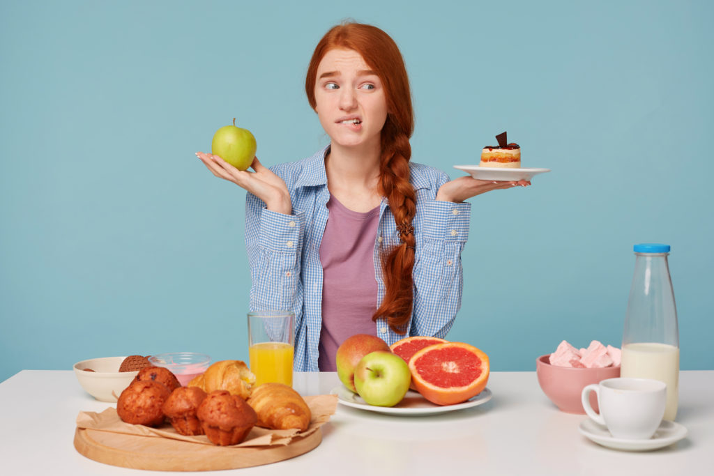 Escolha dificil, mulher ruiva e bonita está tentando decidir entre comer uma maçã e uma torta. hábitos saudaveis