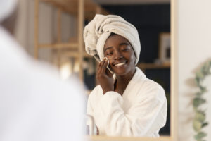 mulher negra fazendo tratamento de beleza e autocuidado, ela está com toalha na cabeça e vestindo roupão