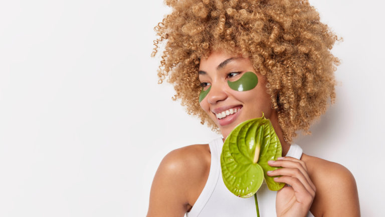 tratamento eficaz de beleza mulher positiva com cabelo loiro encaracolado segura flor de calla desvia o olhar e aplica adesivos de hidrogel verdes vestidos com camiseta isolada sobre fundo branco em branco