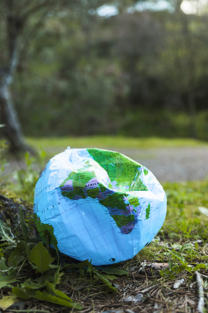 globo terrestre de papel amassado e destruido deitado no chao verde de grama, sustentabilidade